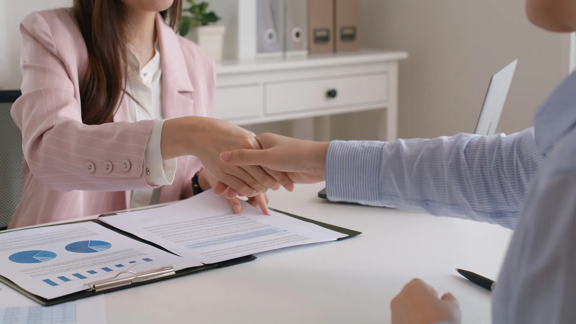 Two professionals shaking hands across a desk.