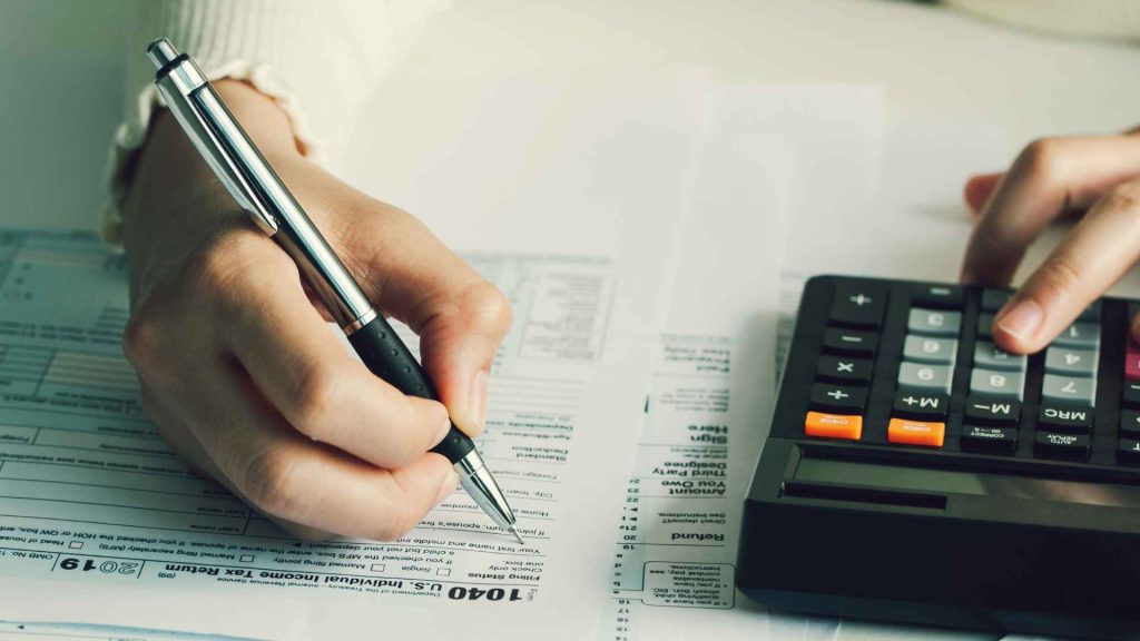 a person with a pen and calculator sitting at a desk