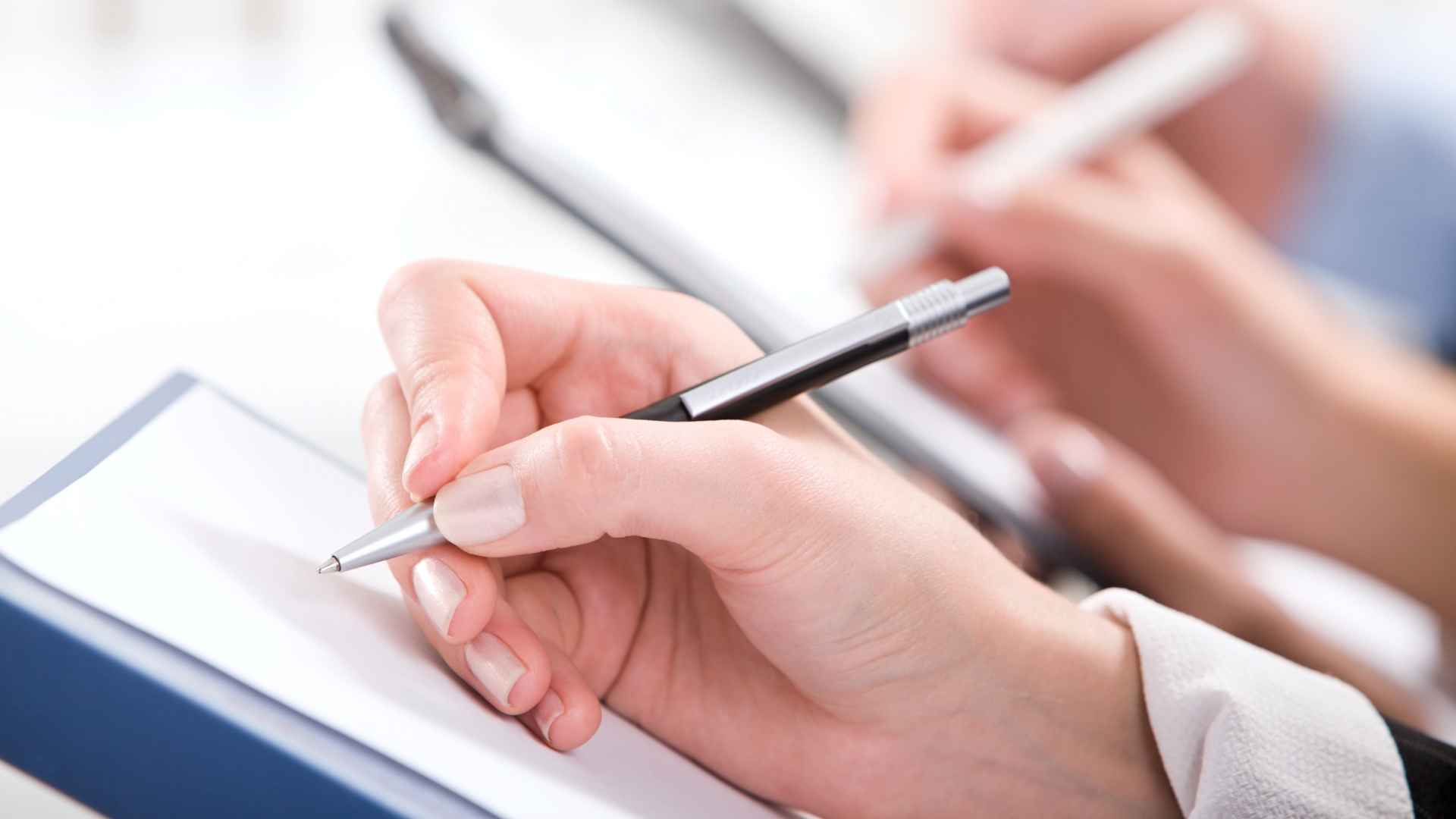 a person holding a pen and writing on a piece of paper